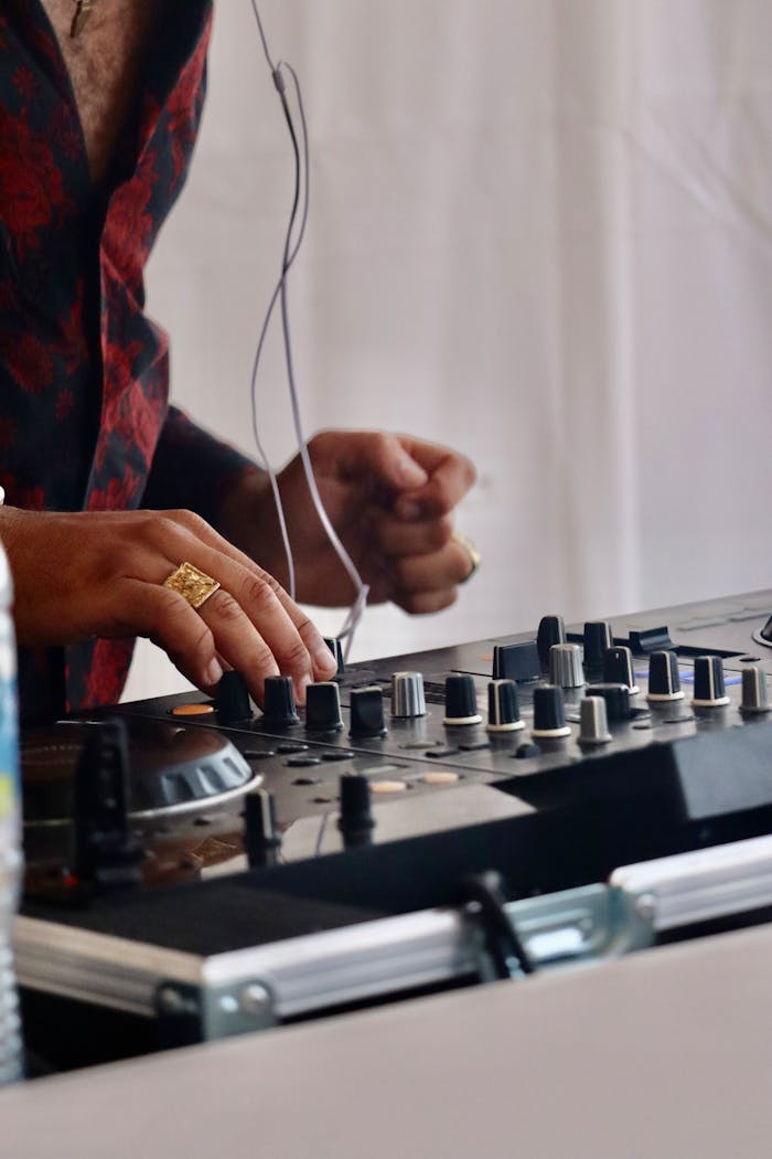 Close-up of a DJ using an audio mixer, adjusting knobs at a lively event.
