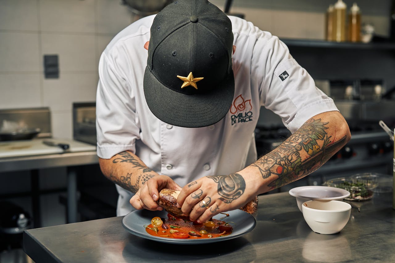 Tattooed chef expertly plates a gourmet dish with precision and skill in a restaurant kitchen.
